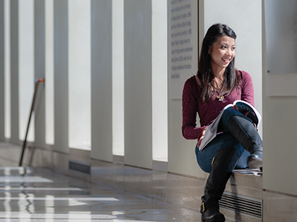 Female student sitting holding a text book staring out the window and smiling